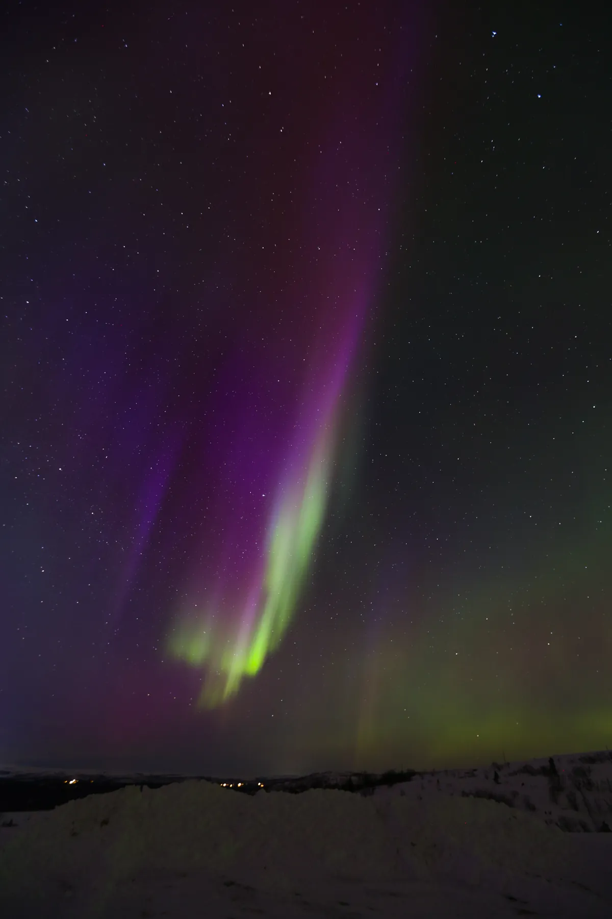 Violet and green aurora streaming overhead above snowy hills