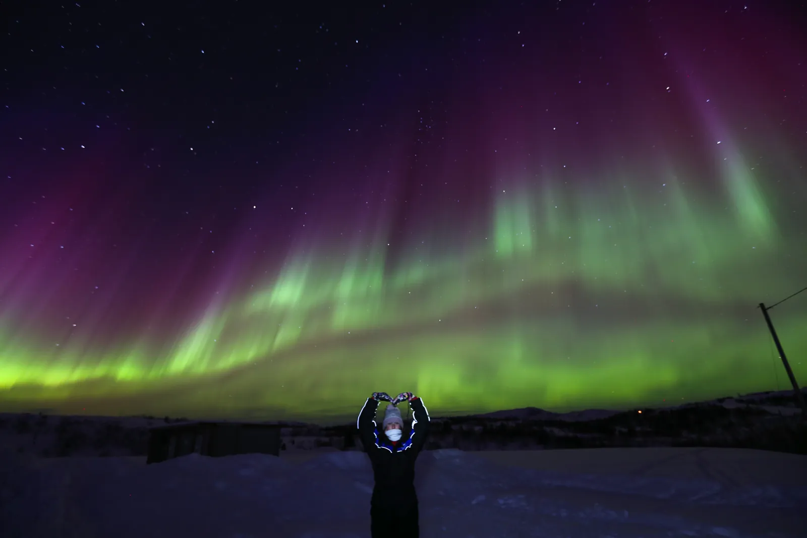 A guest with a headlamp under a wide green and violet aurora arc