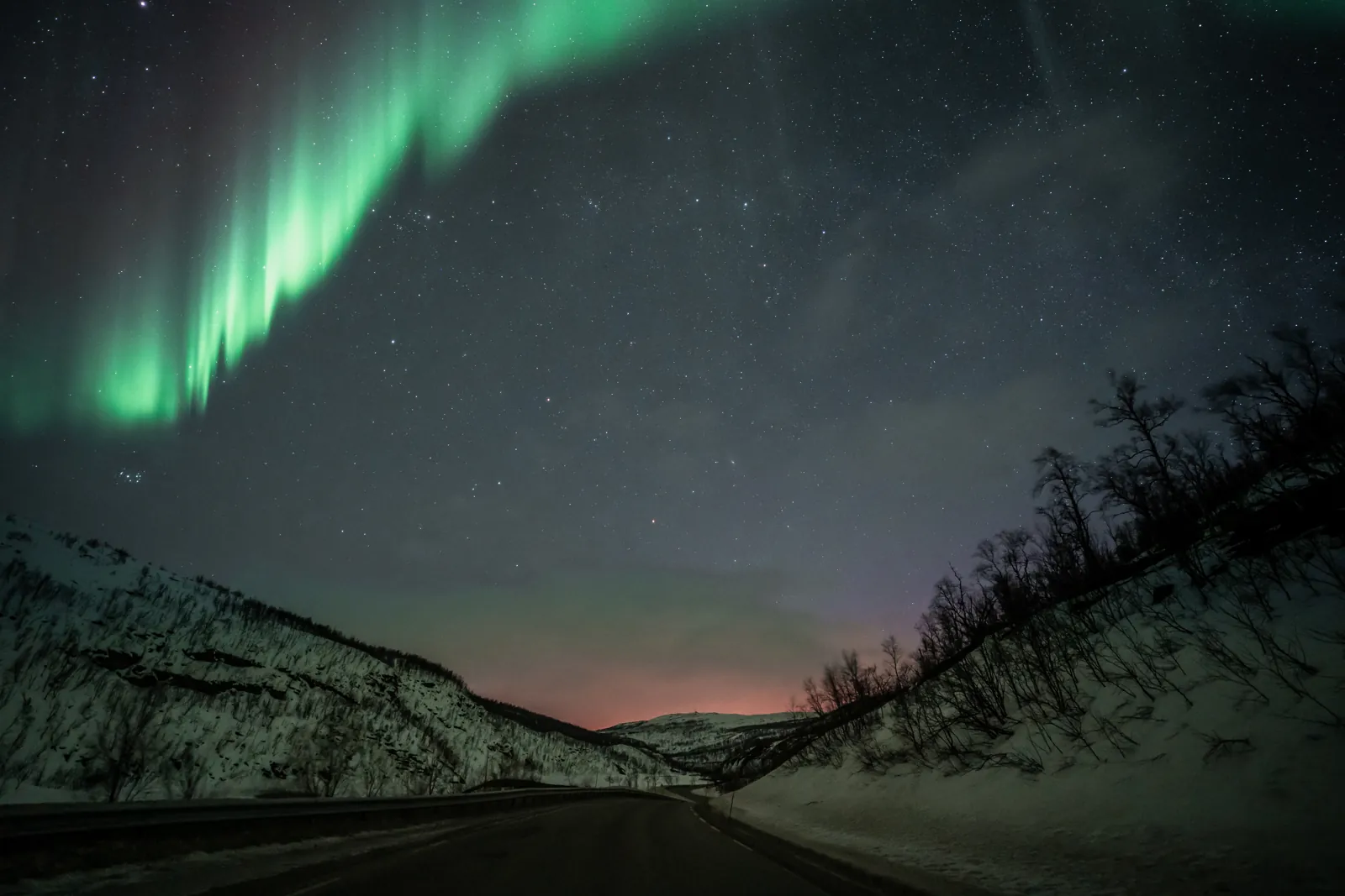 Green aurora over a road winding through a snowy valley
